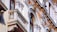 A detailed view of architectural elements on a building facade, featuring ornate decor and intricate stonework. The structure includes archways, columns, and balustrades with classical flourishes and detailed carvings.