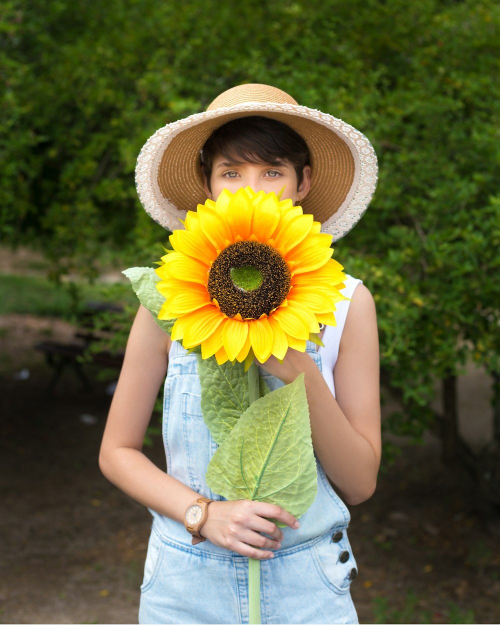 girl in yellow sun hat and green tank top holding sunflower