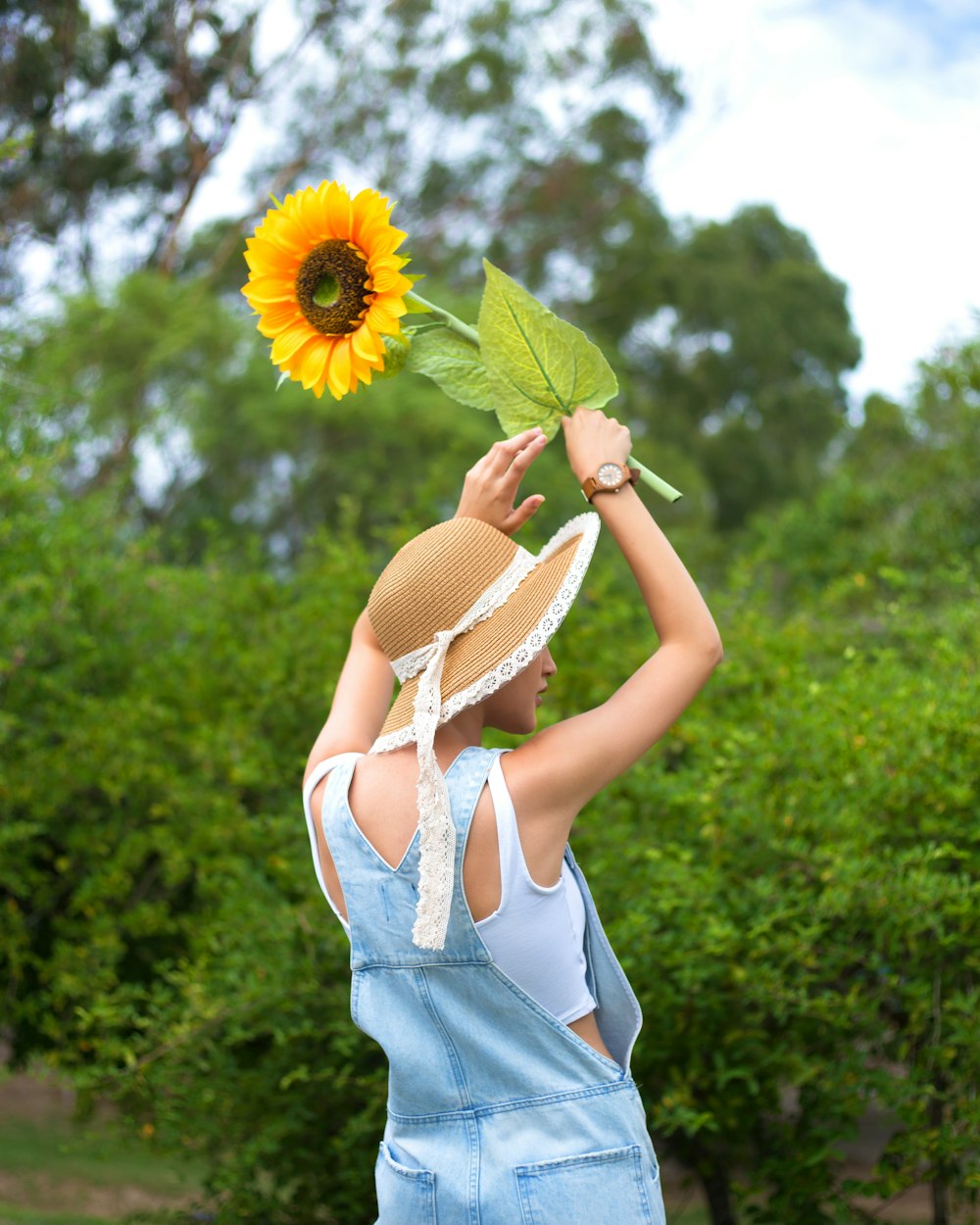 woman in white sleeveless dress holding sunflower during daytime