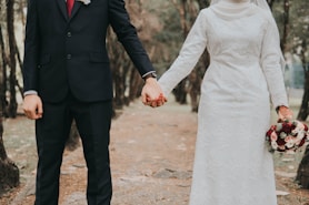 man in black suit jacket and woman in white dress holding hands