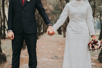 man in black suit jacket and woman in white dress holding hands