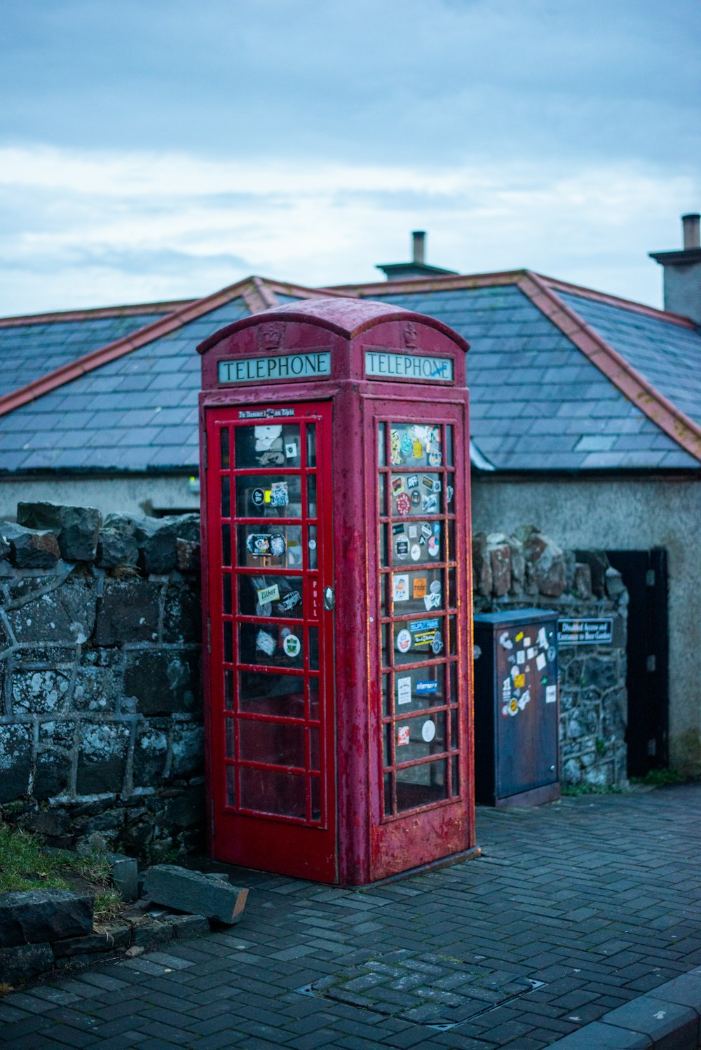 red telephone booth beside gray brick wall