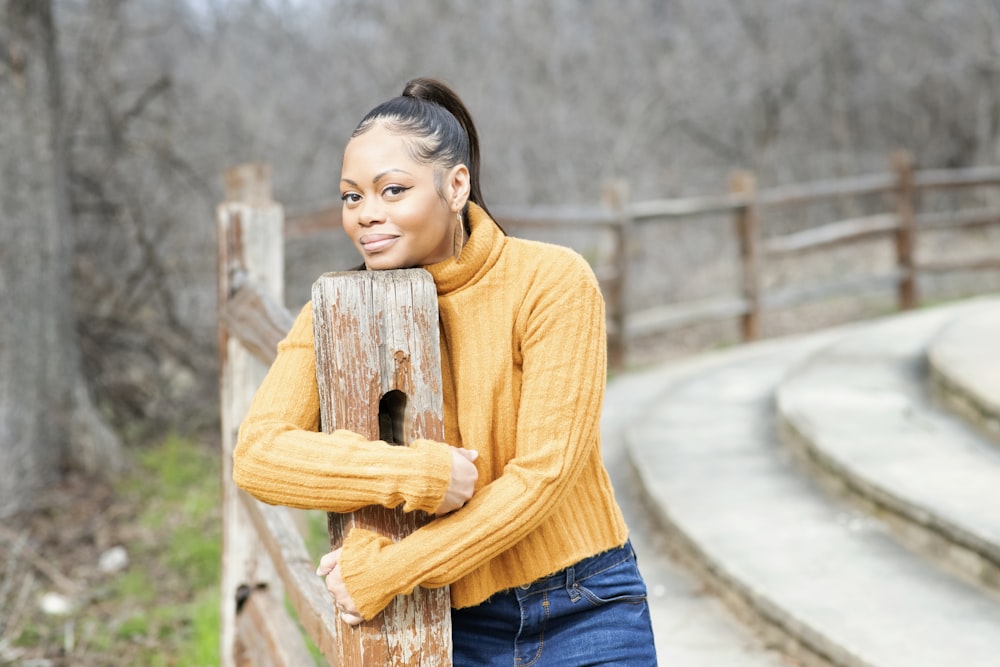 Frau in gelbem Rollkragenpullover und blauer Jeans mit braunem Holzpfosten