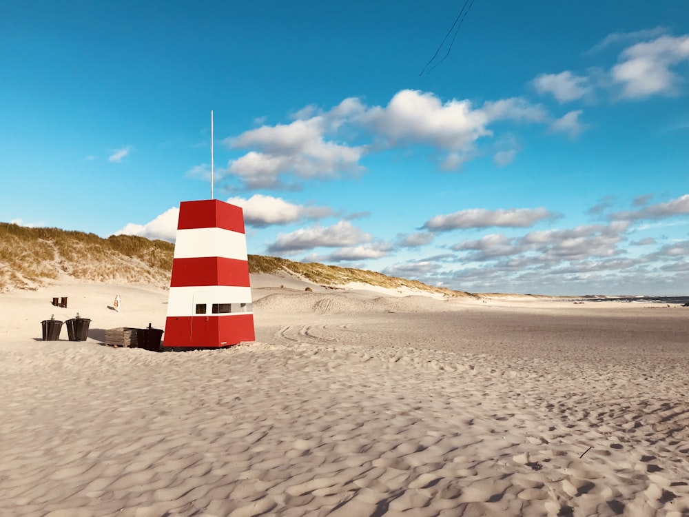 white and red lighthouse on brown sand under blue sky during daytime