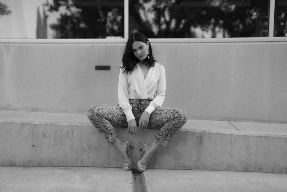 woman in white long sleeve shirt and black pants sitting on concrete floor