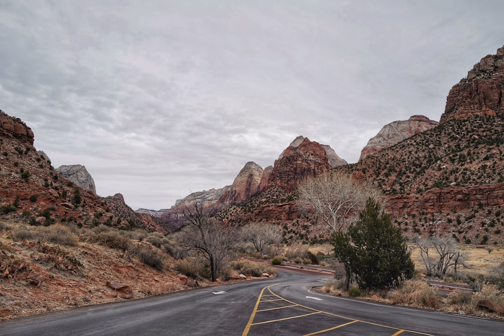 gray concrete road near brown rocky mountain under white sky during daytime