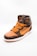 A stylish high-top sneaker featuring a combination of brown and orange tones with a luxurious pattern. The shoe has orange laces and a prominent swoosh logo on its side. The material appears textured, giving off an expensive and designer look. The sneaker is positioned against a plain, light background, highlighting its design.