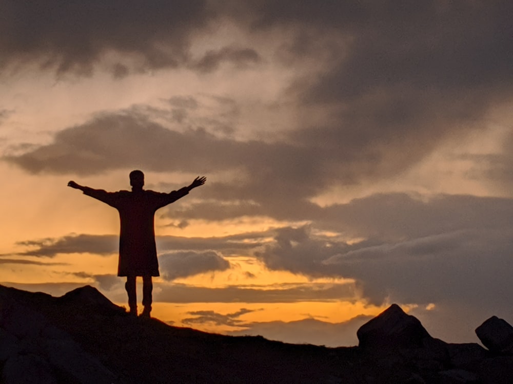 silhouette of man standing on top of mountain during sunset