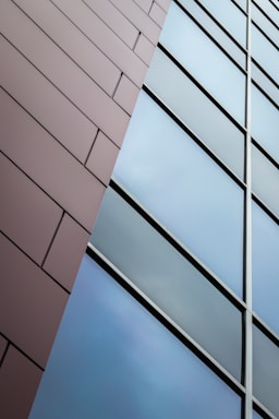 A modern architectural design featuring a close-up view of a building facade with two distinct sections. One side is a textured surface with horizontal linear patterns, and the other side consists of reflective glass panels in a clean, geometric arrangement.