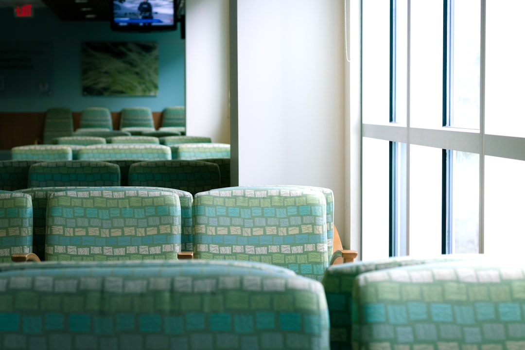 green and white sofa chairs, hospital waiting room with green seats next to bright windows and a TV in the distance