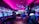 A vibrant arcade with rows of gaming machines adorned with colorful screens. Several people are immersed in playing games, seated on stools in a dimly lit room accented by an intense pink ceiling light. The atmosphere is lively and engaging.