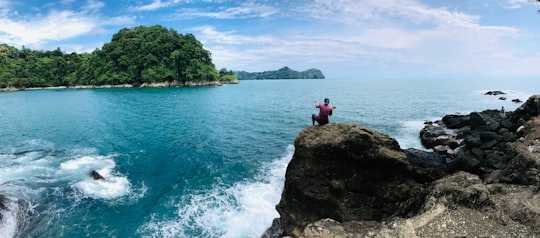 2 person sitting on rock formation near body of water during daytime in Provincia de Puntarenas Costa Rica