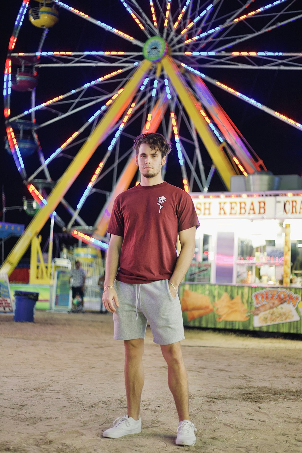 boy in red crew neck t-shirt standing near blue yellow and red ferris wheel during