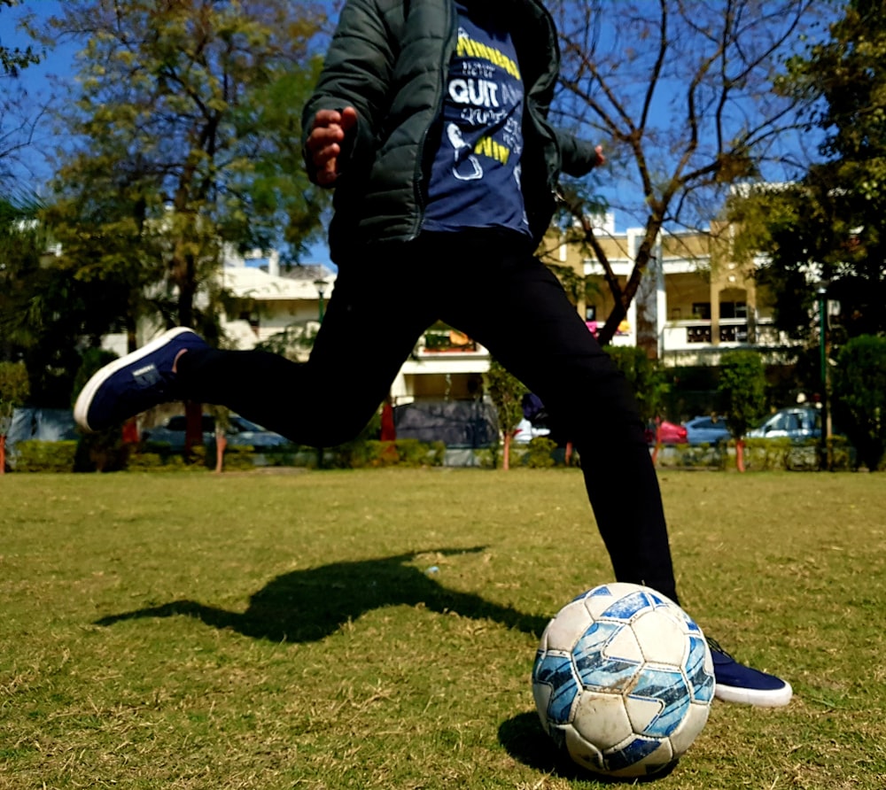 파란색과 흰색 아디다스 긴팔 셔츠와 검은 바지를 입은 남자가 낮에 축구를 하고 있다