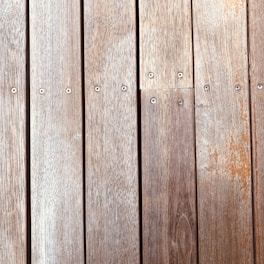 Wooden planks aligned vertically, featuring a natural wood grain and small evenly spaced screws securing them in place. The texture and color of the wood suggest aging, with slight wear and discoloration visible on the surface.
