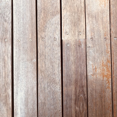 Wooden planks aligned vertically, featuring a natural wood grain and small evenly spaced screws securing them in place. The texture and color of the wood suggest aging, with slight wear and discoloration visible on the surface.