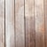 Wooden planks aligned vertically, featuring a natural wood grain and small evenly spaced screws securing them in place. The texture and color of the wood suggest aging, with slight wear and discoloration visible on the surface.