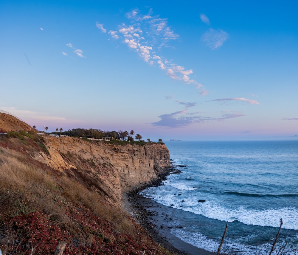 green grass on brown rocky mountain beside blue sea under blue and white cloudy sky during