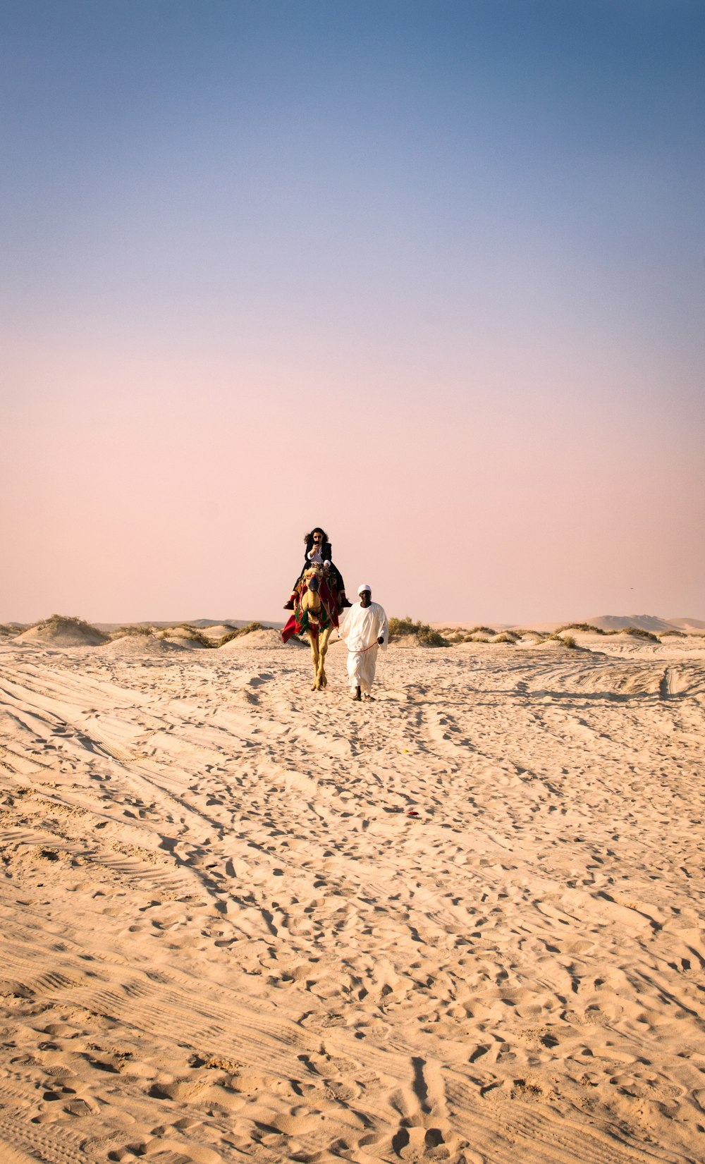 흰색 긴 소매 셔츠와 검은 바지를 입은 여자가 낮에 갈색 모래 위를 걷고 있다