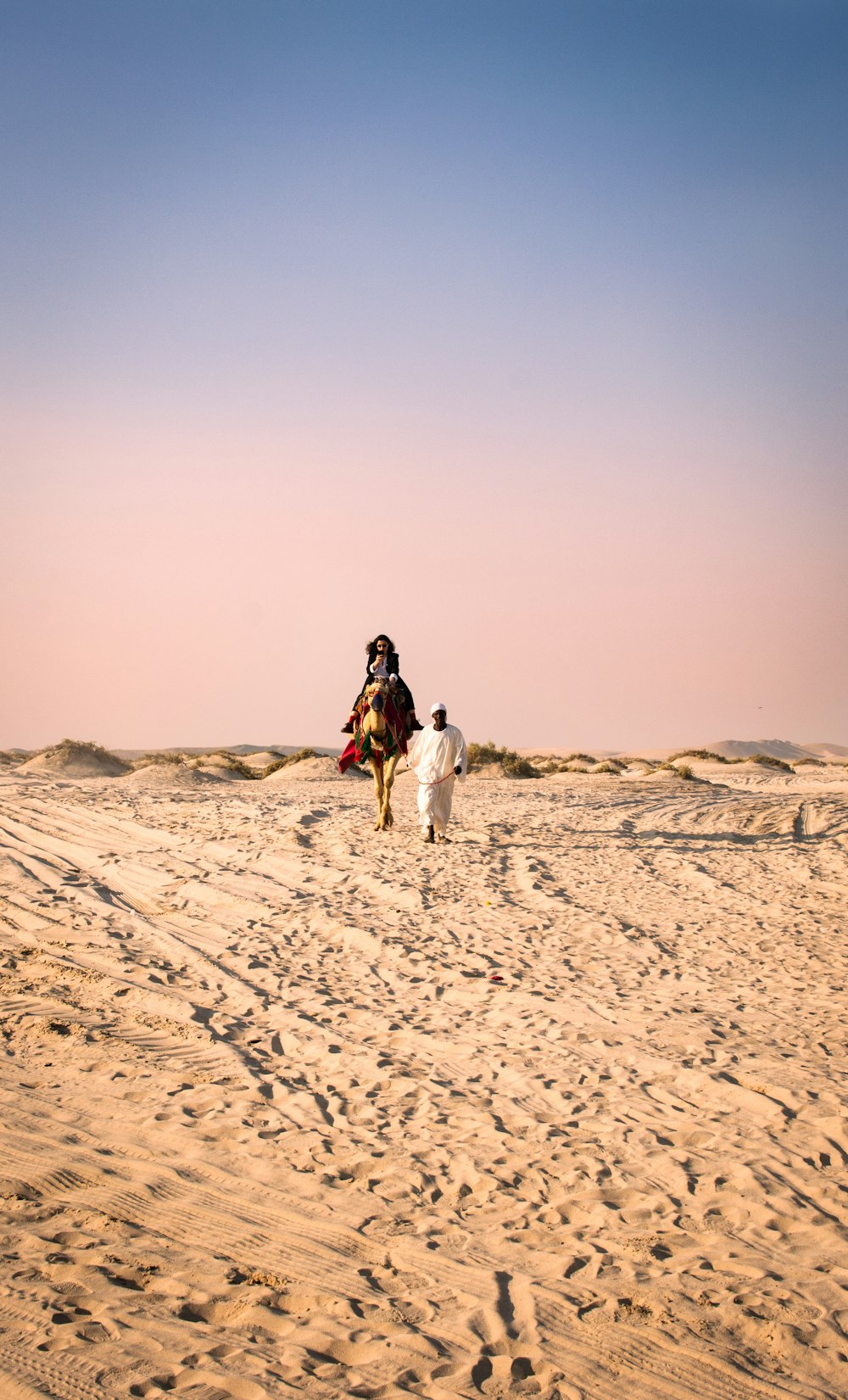 woman in white long sleeve shirt and black pants walking on brown sand during daytime