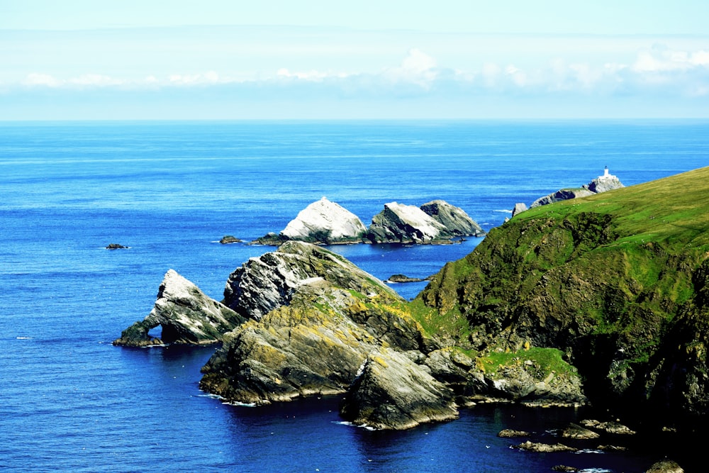 green and gray rock formation beside blue sea under blue sky during daytime