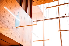 A modern interior with large windows and wooden paneling featuring suspended linear lights. A subtle light blue bottle silhouette is present on a perforated white panel wall.