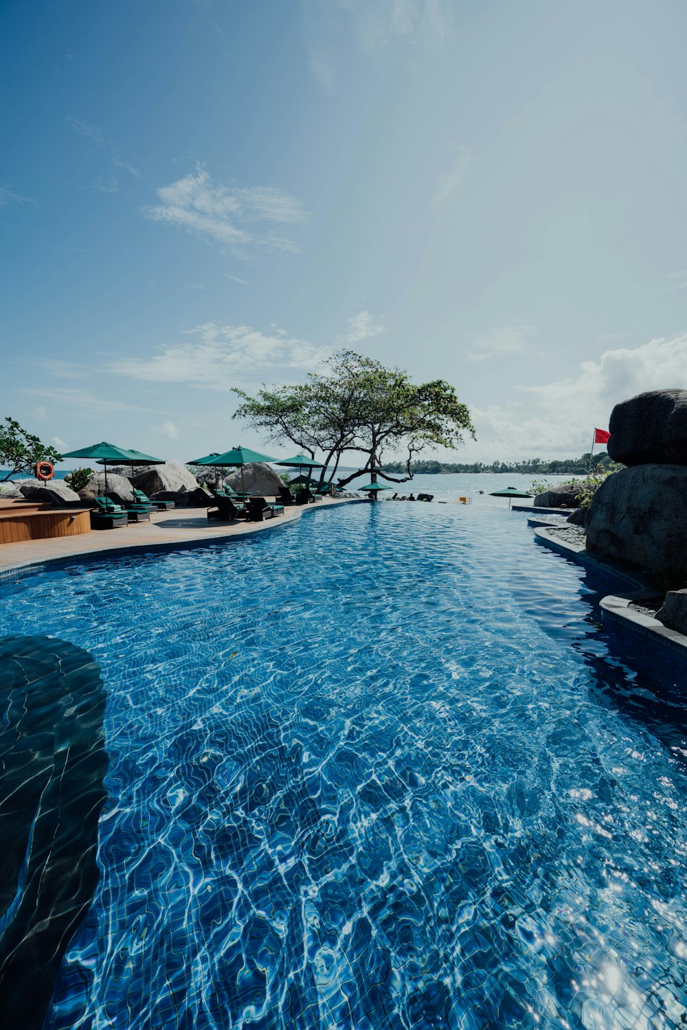 man in black jacket sitting on black rock near swimming pool during daytime