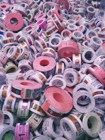 A collection of colorful tickets or coupons rolled into cylinders, with various denominations and text visible on each roll. The tickets are stacked in a chaotic and overlapping manner, showcasing a range of colors and patterns.