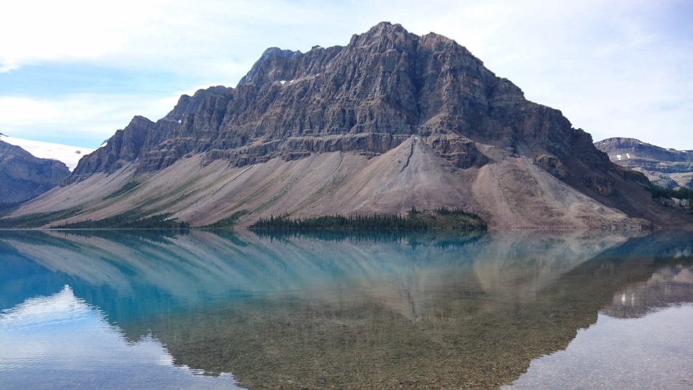 blue lake near brown and gray mountain under white sky during daytime