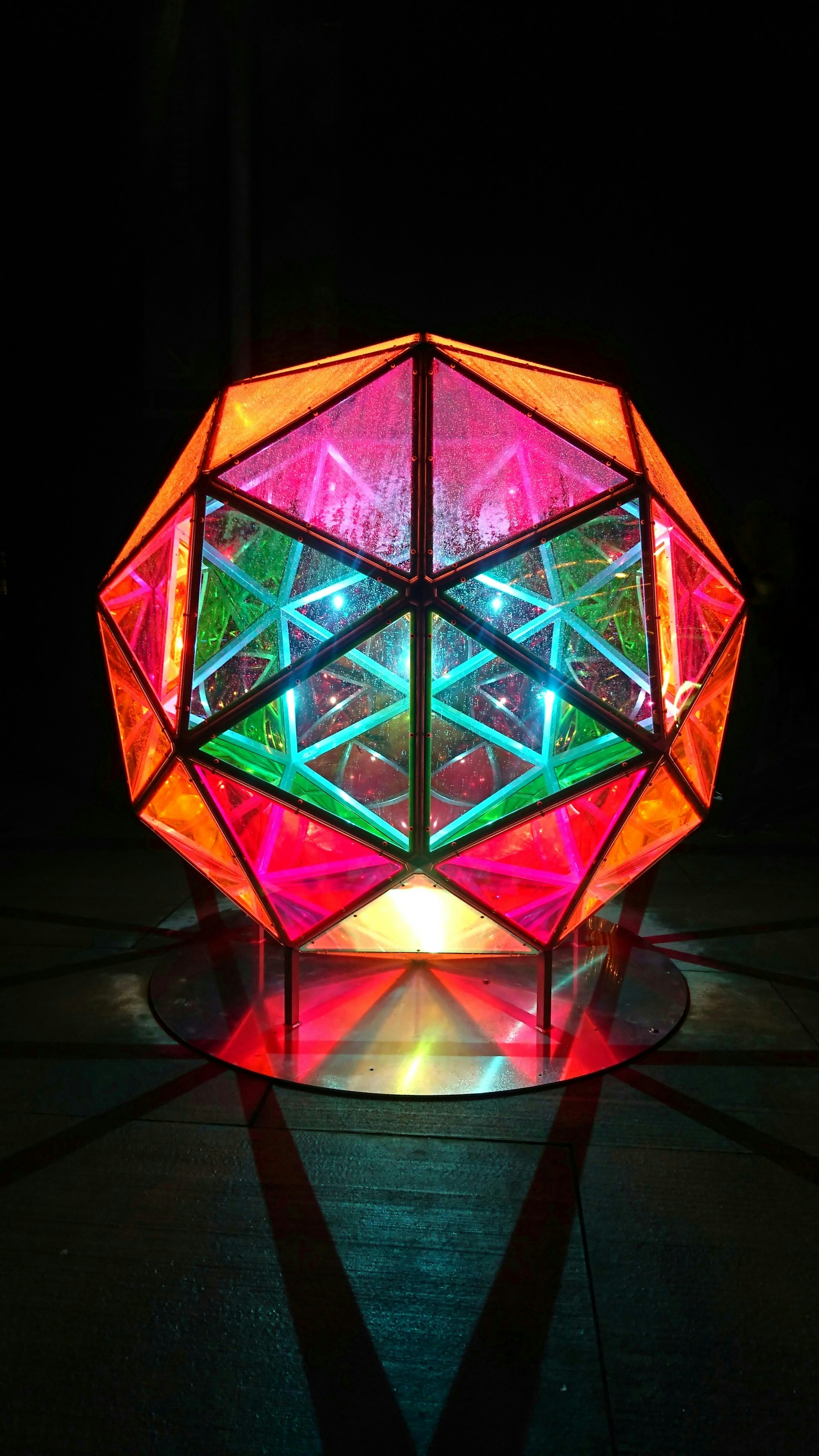 A vibrant 3D printed sculpture with intricate geometric patterns glowing under colorful LED lights.