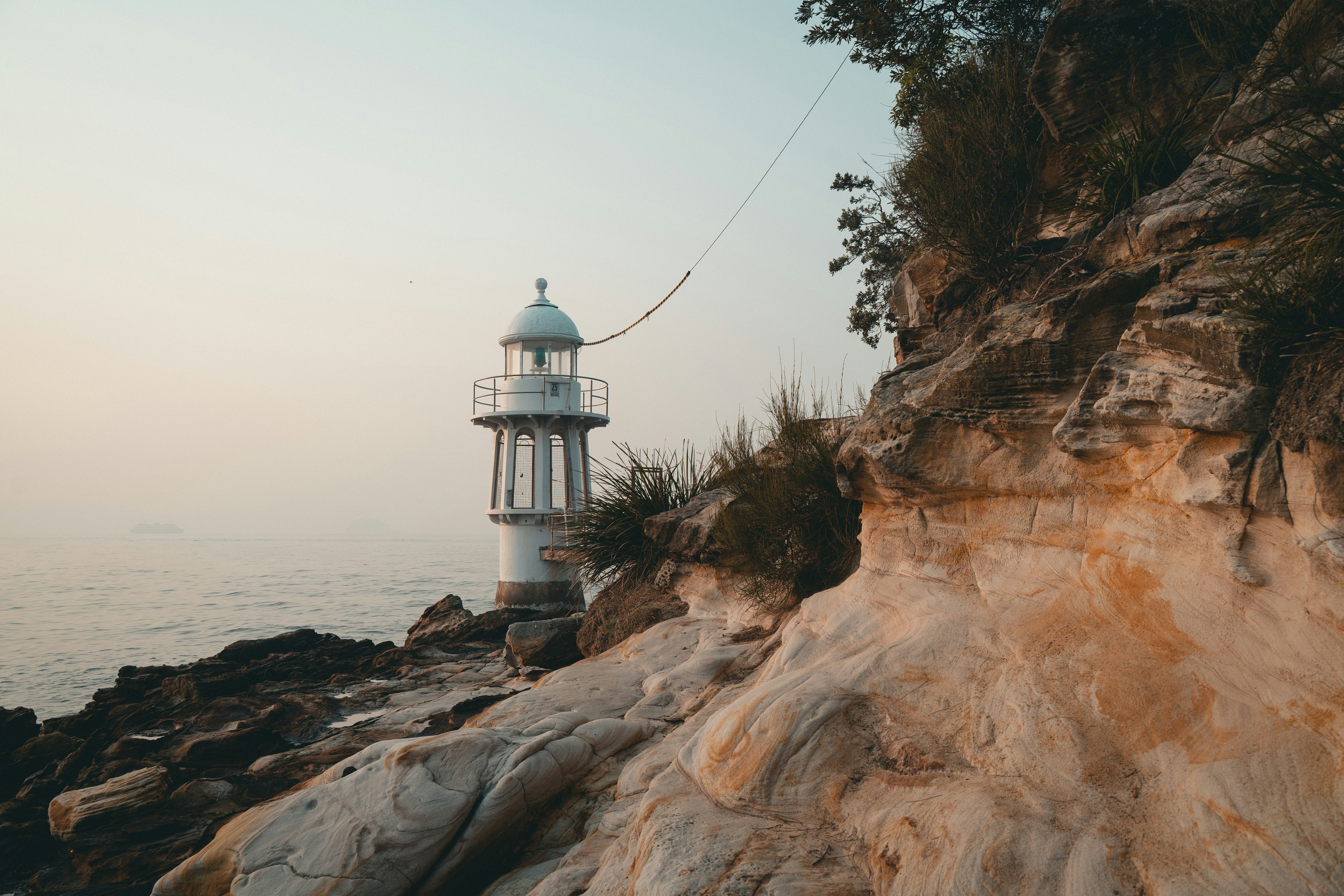 White and black lighthouse on brown rock formation near body of water ...
