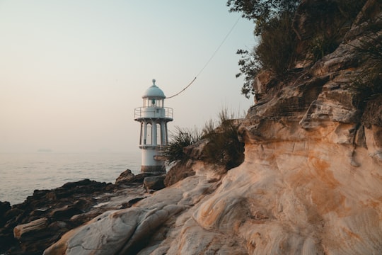 white and black lighthouse on brown rock formation near body of water during daytime in Cremorne Point NSW Australia