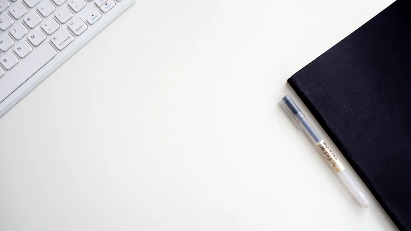 Minimalist workspace with a notebook, pen, and a cup of coffee on a white desk.