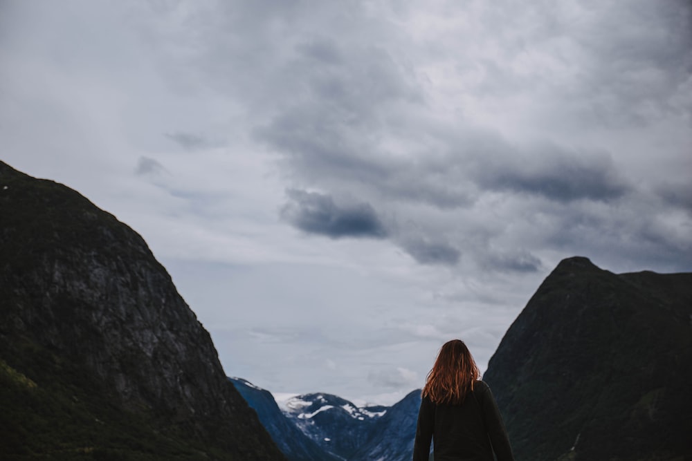 mulher na jaqueta preta de pé na montanha durante o dia