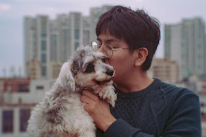 A happy pet parent hugging their dog dressed in a cute, handmade hoodie on a city street.