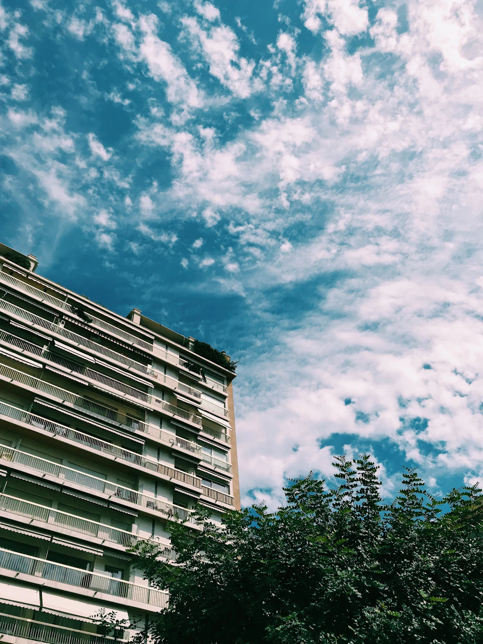 Tall white apartment building with multiple levels and balconies under clear blue sky