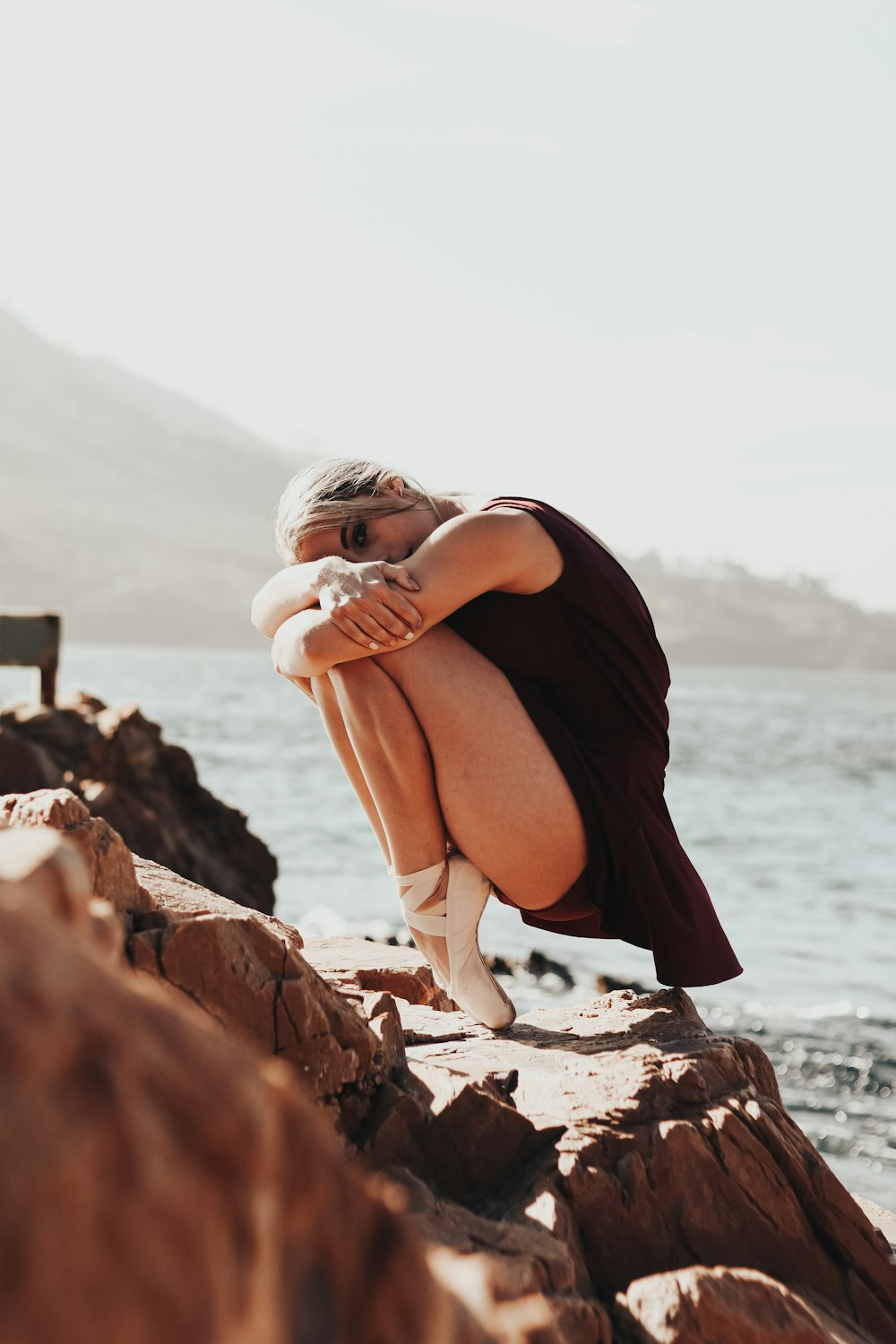 woman in black dress sitting on rock near sea during daytime