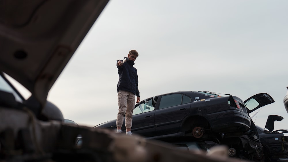 man in black jacket and brown pants standing beside black car during daytime