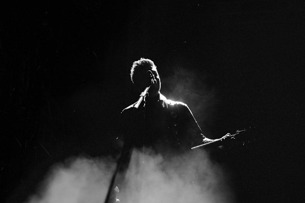 man singing on stage in grayscale photography
