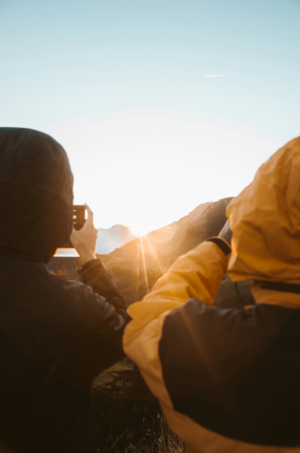 man in yellow jacket and black knit cap sitting on rock during daytime