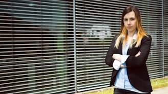 woman in black blazer standing near window blinds