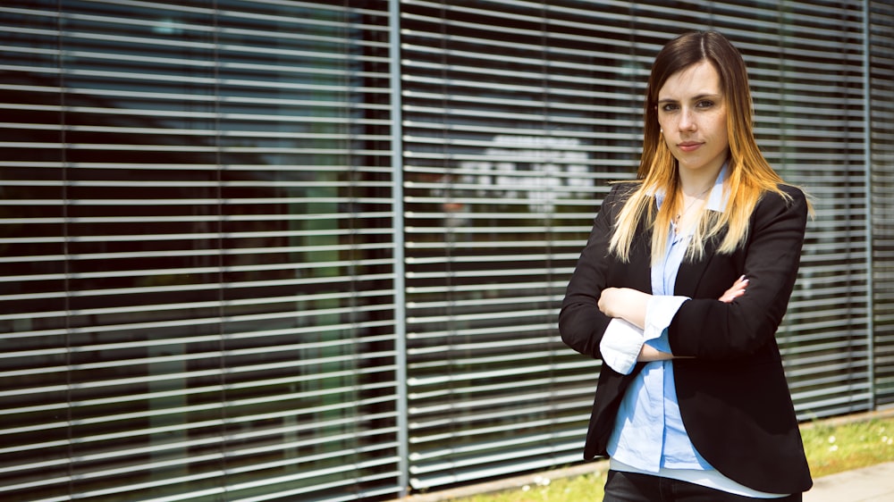 woman in black blazer standing near window blinds