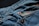 Close-up view of blue denim fabric with a focus on a pocket that features a red logo tag. Copper rivets are visible, highlighting the stitching and texture of the material.