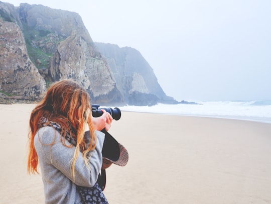 woman in brown jacket taking photo of sea during daytime in Colares Portugal