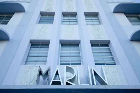 A building facade featuring multiple vertically aligned windows with bars and decorative panels in between. A large sign with the text 'MARLIN' is prominently displayed at the bottom.