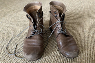 A pair of classic brown leather boots resting on a worn wooden floor.