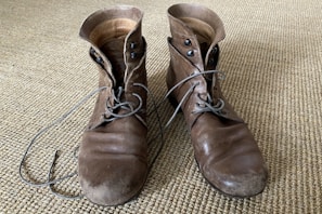 A stylish pair of brown leather boots on a rustic wooden floor.