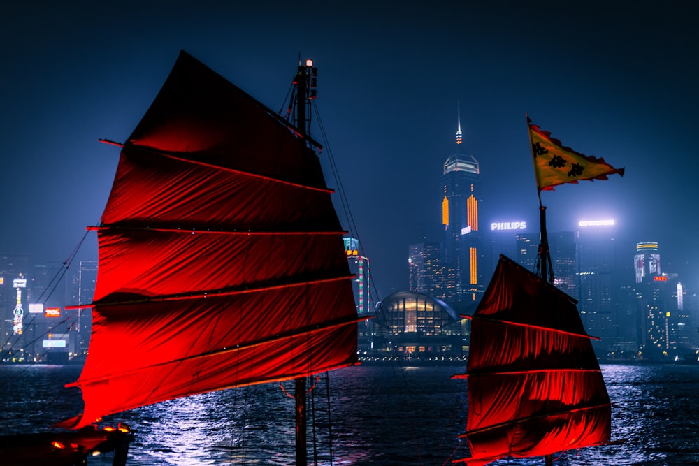 red sail boat on body of water near city buildings during night time