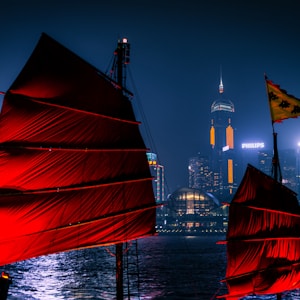 red sail boat on body of water near city buildings during night time