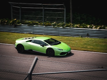 A bright green sports car drives swiftly along a racetrack surrounded by metal barriers. The setting suggests a professional racing environment with a clear, focused path. The car is sleek, aerodynamic, and appears to be a high-performance model.